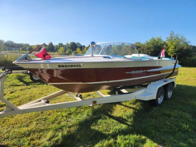 Vintage wooden Chris-Craft boat on a trailer in sunlight.